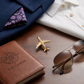 Gold airplane brooch with pilot logbook and sunglasses flatlay