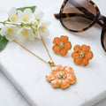 Parure fleur or et émail orange pêche sur marbre blanc avec fleurs de jasmin et lunettes de soleil