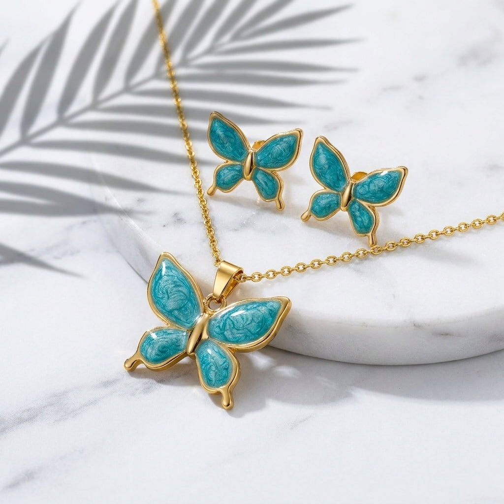 Parure papillon or et émail turquoise - collier pendentif et boucles d'oreilles sur marbre blanc avec feuille de palmier